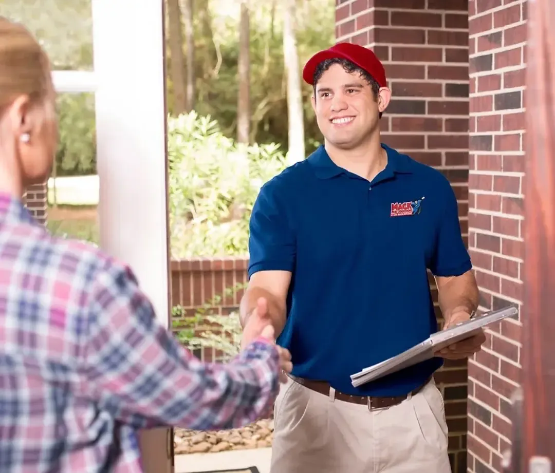 Mack Pest Solutions technician in uniform greeting a happy customer at their door